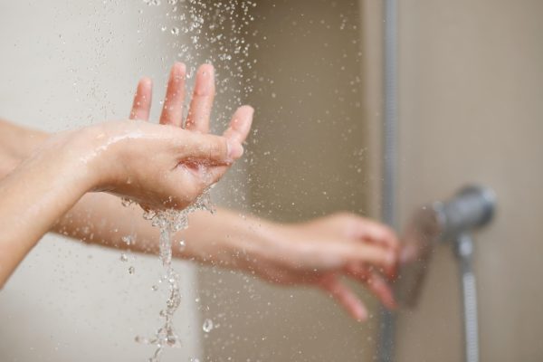 woman uses hand measure water temperature from water heater before taking shower -