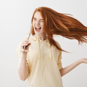 happy redhead girl playing karaoke app game smartphone singing song earphones -